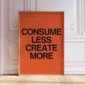 Peut inclure: Une affiche encadrée avec un fond orange et un texte noir qui dit "CONSUMER MOINS CRÉER PLUS".