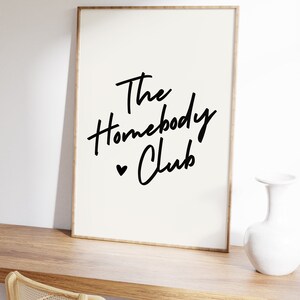 Cream background with The HomebodyClub written in black cursive 
 font with a black heart