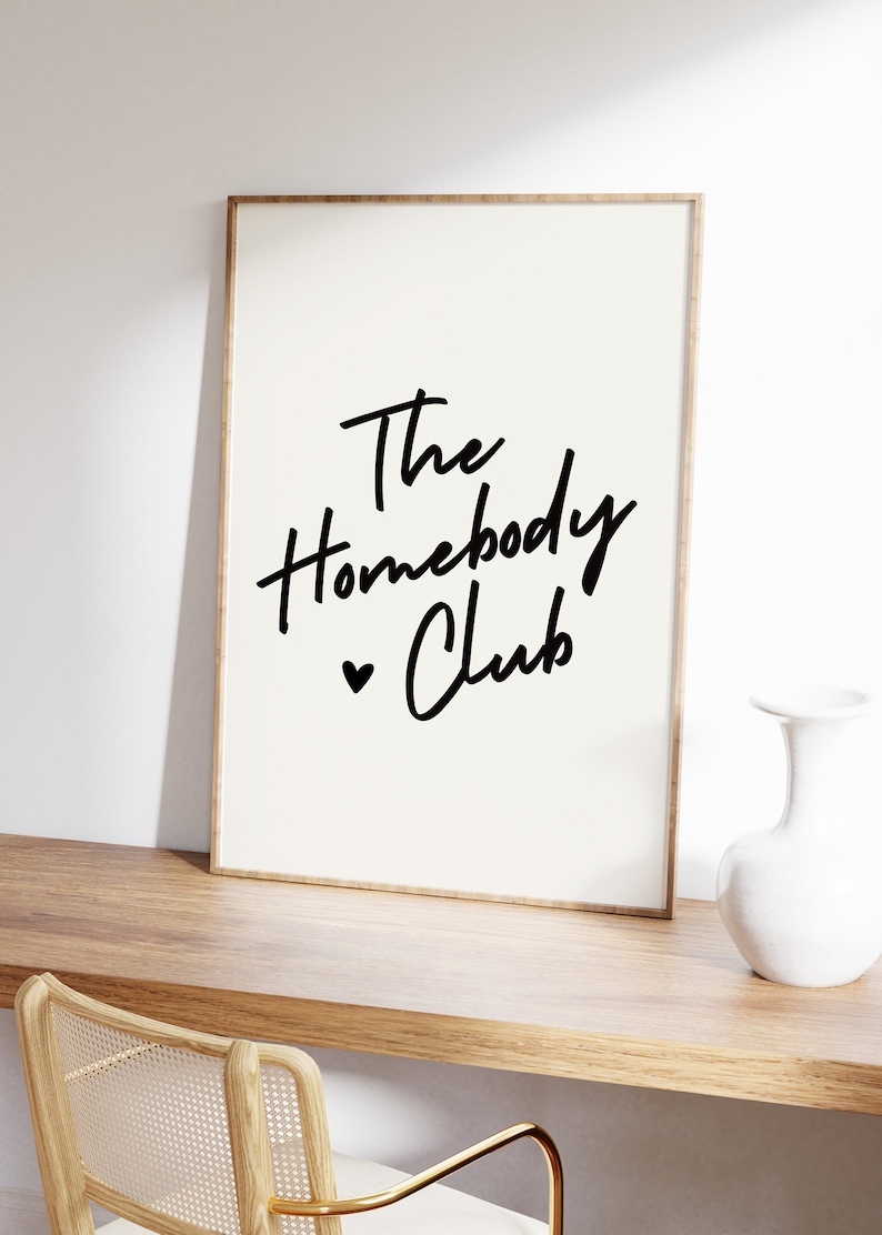 Cream background with The HomebodyClub written in black cursive 
 font with a black heart