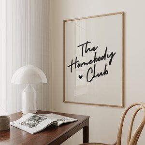 Cream background with The HomebodyClub written in black cursive 
 font with a black heart