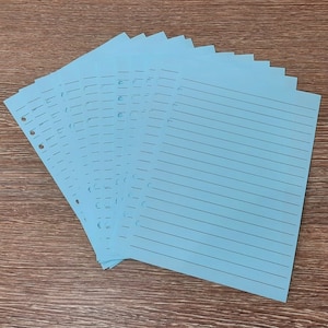 May include: A stack of light blue lined paper with holes punched along the left edge. The paper is designed for use in a binder.