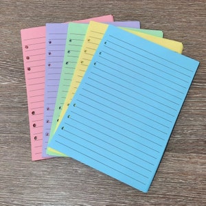 May include: A stack of five lined paper sheets in different pastel colours: pink, lavender, light green, yellow, and light blue. The sheets are punched with holes on the left side for a binder.