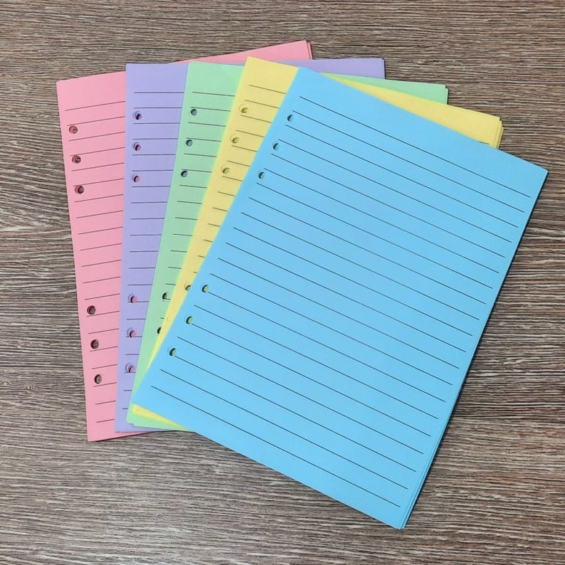 May include: A stack of five lined paper sheets in different pastel colors: pink, lavender, light green, yellow, and light blue. The sheets are punched with holes on the left side for a binder.