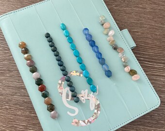 May include: A light blue binder with five rows of beads. The beads are in different colors and patterns, including turquoise, blue, and brown.