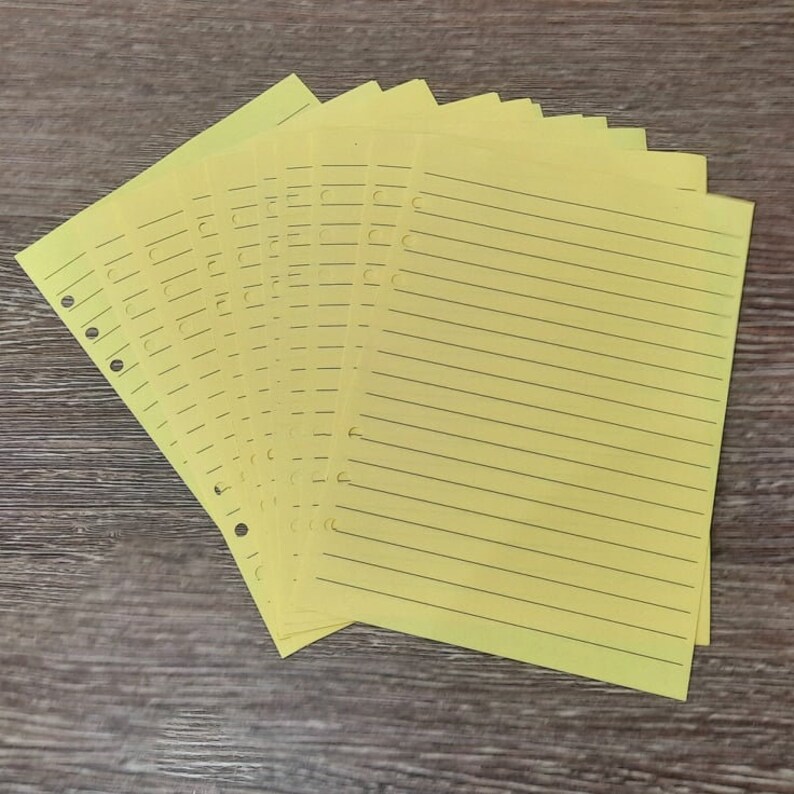 May include: A stack of yellow lined paper with holes punched along the left edge. The paper is designed for use in a binder.
