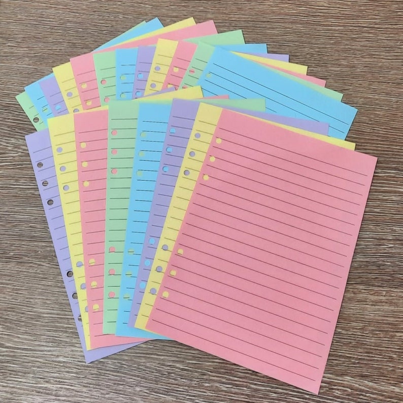 May include: A stack of colorful lined paper with punched holes for a binder. The paper is in shades of pink, yellow, blue, and green.