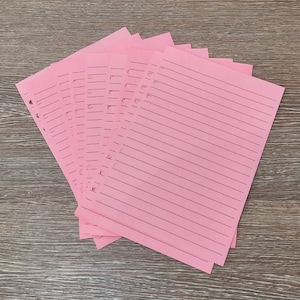 May include: A stack of pink lined paper with holes punched along the left edge. The paper is folded in a fan shape.