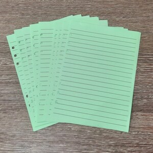 May include: A stack of light green lined paper with holes punched along the left edge. The paper is designed for use in a binder.
