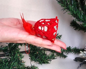 May include: A red crocheted bell ornament with a red ribbon bow. The bell is decorated with small red beads.
