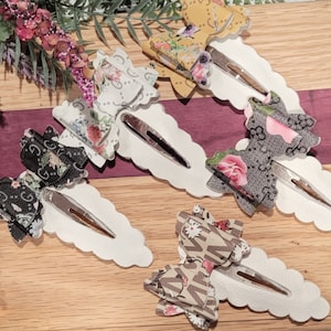 May include: Four hair clips with white bases and different patterned bows. The bows are black and white, brown and white, yellow and white, and pink and white.