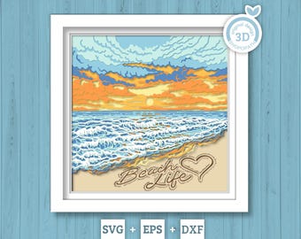 May include: A layered paper-cut style artwork in a white frame depicting a beach sunset with orange and yellow clouds, blue ocean waves, and tan sand. The text Beach Life and a heart outline are visible on the sand. A 3D design badge is in the corner.