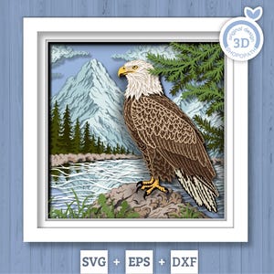 May include: 3D layered art piece featuring a bald eagle perched on a rock near a river, with mountains in the background. The eagle has brown and white feathers, a yellow beak, and yellow talons. The artwork is framed in a white square frame. The image includes the text "SVG + EPS + DXF".