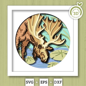 May include: A layered paper art piece depicting a moose drinking from a pond. The moose is brown with large antlers, and the pond has lily pads. The artwork is set in a white square frame, with the text "SVG + EPS + DXF" at the bottom.