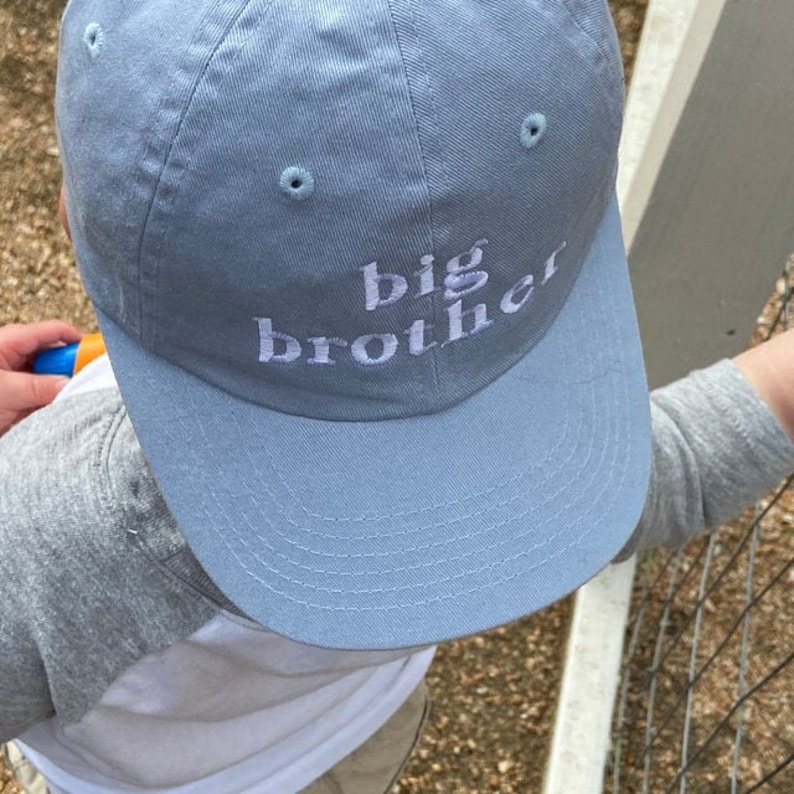 May include: A light blue baseball cap with the words "big brother" embroidered in white on the front.