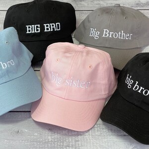 Puede incluir: Cinco gorras de b&eacute;isbol de diferentes colores con texto bordado. Las gorras son azules, rosas, grises, negras y negras. El texto en las gorras dice "big bro", "big sister", "Big Brother", "BIG BRO" y "big brother".