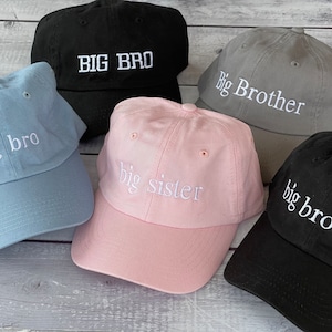 Puede incluir: Cinco gorras de b&eacute;isbol con texto bordado. Las gorras son de varios colores, incluyendo negro, gris, azul claro, rosa y azul oscuro. El texto en las gorras dice "Big Bro", "Big Brother", "big bro", "big sister" y "big brother".