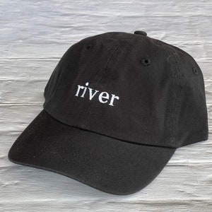 Puede incluir: Una gorra de b&eacute;isbol negra con la palabra "river" bordada en blanco en la parte delantera.