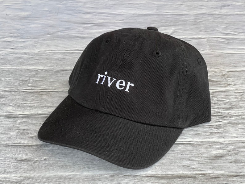 Puede incluir: Una gorra de b&eacute;isbol negra con la palabra "river" bordada en blanco en la parte delantera.