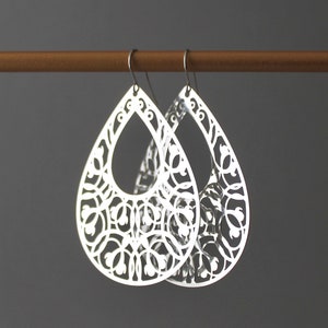 May include: A pair of silver teardrop-shaped earrings with a delicate, intricate floral design.