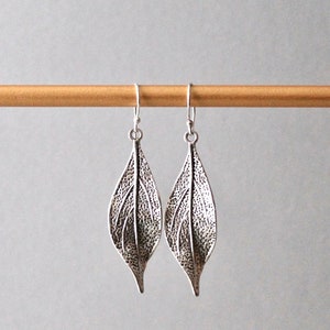 May include: A pair of silver leaf-shaped dangle earrings. The earrings are made of metal and have a textured surface.