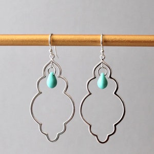 May include: Silver dangle earrings with a turquoise teardrop charm. The earrings have a delicate, ornate design.