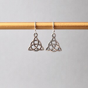 May include: A pair of silver earrings with a Celtic knot design. The earrings are hanging from a gold rod.