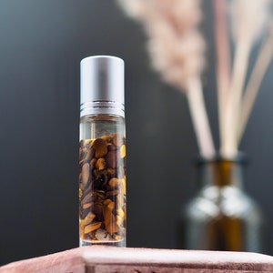 Peut inclure: Un flacon en verre transparent avec un bouchon en argent rempli de cristaux bruns et dorés. Le flacon est posé sur une surface brune.