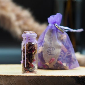 Puede incluir: Un pequeño frasco de vidrio lleno de hierbas y flores secas, sellado con un tapón de cera morado. El frasco está sentado sobre una superficie de madera junto a una bolsa de cordón morado llena de hierbas y flores similares. La bolsa tiene una etiqueta que dice "psicodélico".