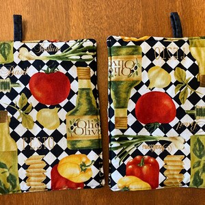 May include: Two black and white checkered kitchen pot holders with a colorful Italian food theme. The pot holders feature images of tomatoes, garlic, basil, green onions, olive oil bottles, and pasta. The text "Pesto" and "Olive Oil" are visible on the pot holders.