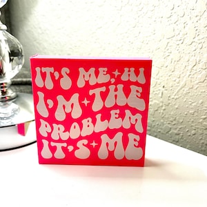 May include: Pink block with white text that reads "It's me, hi I'm the problem it's me".