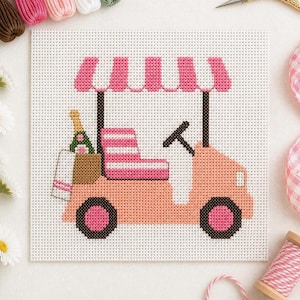 May include: A cross-stitch design of a golf cart in shades of pink and brown. The cart has a striped seat, a canopy, and a steering wheel. A bottle of champagne and a shopping bag are in the back. The wheels are dark brown.