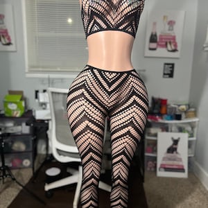 Puede incluir: Conjunto de lencería negra con un patrón geométrico. La parte superior es un top corto con una tela transparente y pedrería. La parte inferior es un pantalón de yoga con una tela transparente.