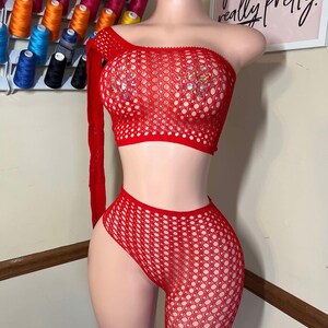 May include: A red, one-shoulder crop top with a long sleeve and matching shorts. The outfit is made of a net-like material and adorned with sparkling embellishments. The text on the wall says "you're like, really pretty."