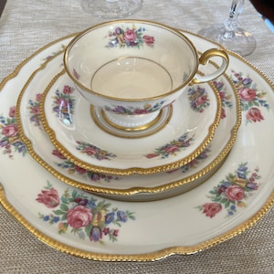 May include: A set of three white porcelain plates with gold trim and floral designs. The plates are nested inside each other, with the smallest plate in the center. The plates have a scalloped edge and a delicate floral pattern in shades of pink, blue, and green.