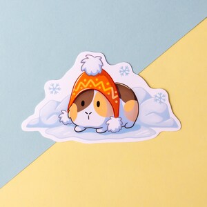 May include: A cartoon illustration of a guinea pig wearing a red and yellow knitted hat, nestled in a bed of white snow. The guinea pig has brown and white fur and is looking to the left.