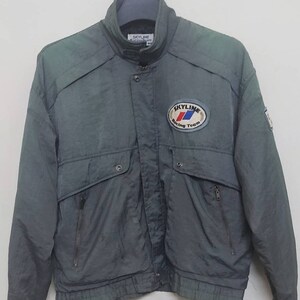 May include: A dark green jacket with a zip fastening and a Skyline Racing Team logo patch on the left chest. The jacket has a stand-up collar and two pockets on the front.