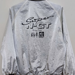 May include: Silver jacket with black trim and the text "Super N-GT Racing Team" in black. The jacket has a collar and long sleeves. The Japanese characters are also in black.