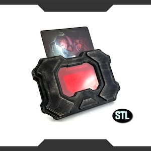 Puede incluir: Una funda rectangular negra y marrón con una pantalla roja que dice "CONTAMINATION". Una tarjeta con un gráfico se inserta en la parte superior. La funda tiene un diseño industrial texturizado. Las letras "STL" están en la esquina inferior derecha.