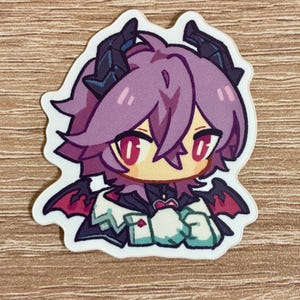 May include: A sticker featuring a cartoon character with purple hair, red eyes, and small black horns. The character has small red and black wings and is wearing a white and teal outfit. The sticker is on a light brown wooden surface.