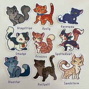 Op de afbeelding: Een verzameling van negen ge&iuml;llustreerde kattenstickers met de personages Graystripe, Rusty, Ravenpaw, Smudge, Princess, Spottedleaf, Bluestar, Dustpelt en Sandstorm. Elke sticker toont een unieke kat in een cartoonstijl.