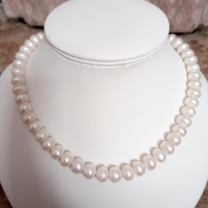May include: A white pearl necklace on a white display stand. The pearls are round and smooth.