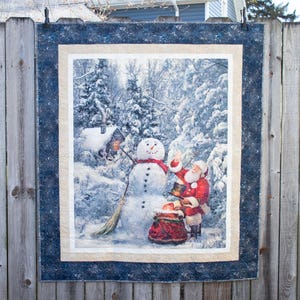 May include: A winter scene with a snowman and Santa Claus in a snowy forest. The snowman is wearing a red scarf and a black top hat. Santa Claus is holding a bag of gifts and a candy cane. The scene is framed by a blue and white border.