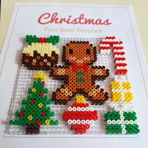 K&ouml;nnte beinhalten: Weihnachts-Perlen-Vorlage mit einem Lebkuchenmann, einem Weihnachtsbaum, einem Zuckerstangen, einem Pudding und einem Ornament. Die Vorlage besteht aus klarem Kunststoff mit einem Gittermuster.