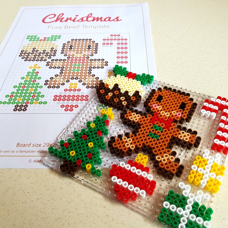 K&ouml;nnte beinhalten: Eine transparente Perlenplatte aus Kunststoff mit Weihnachtsmotiv. Die Platte zeigt einen Lebkuchenmann, einen Weihnachtsbaum, einen Zuckerstock und einen Weihnachtspudding. Die Platte ist 29 Zoll mal 29 Zoll gro&szlig;.