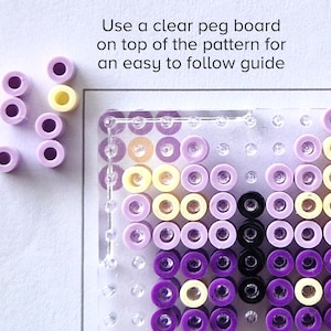 May include: A close-up of a clear peg board with purple, yellow, and black beads arranged in a butterfly pattern. The text "Use a clear peg board on top of the pattern for an easy to follow guide" is visible above the board.