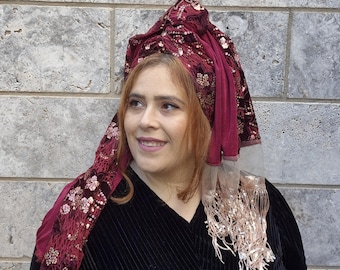 May include: A burgundy velvet head covering with gold sequins and a gold fringe. The head covering is worn by a person with red hair.