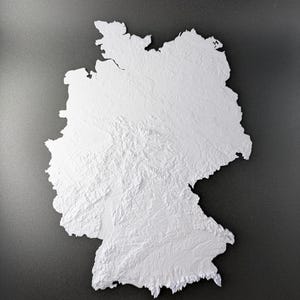 Könnte beinhalten: Eine weiße, dreidimensionale Reliefkarte von Deutschland, die die geografischen Merkmale des Landes zeigt. Die Karte ist vor einem dunkelgrauen Hintergrund platziert und hebt die detaillierten Konturen und Texturen des Geländes hervor.