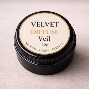 Può includere: Un barattolo cosmetico nero e rotondo con bordo dorato ed etichetta color crema. L'etichetta recita "VELVET DIFFUSE Veil" in un carattere serif, con "30g" sotto. Le parole "SMOOTH - REFINE - PERFECT" sono stampate attorno al bordo inferiore dell'etichetta.