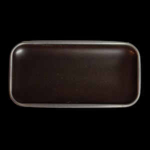 Puede incluir: Una caja rectangular de metal marrón oscuro con esquinas redondeadas y un borde plateado. La caja está sobre un fondo negro, resaltando su forma y color. La superficie de la caja parece lisa y reflectante.