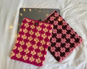 May include: Two crocheted laptop sleeves, one pink and peach, the other brown and pink, with a wooden button on the pink and peach sleeve.